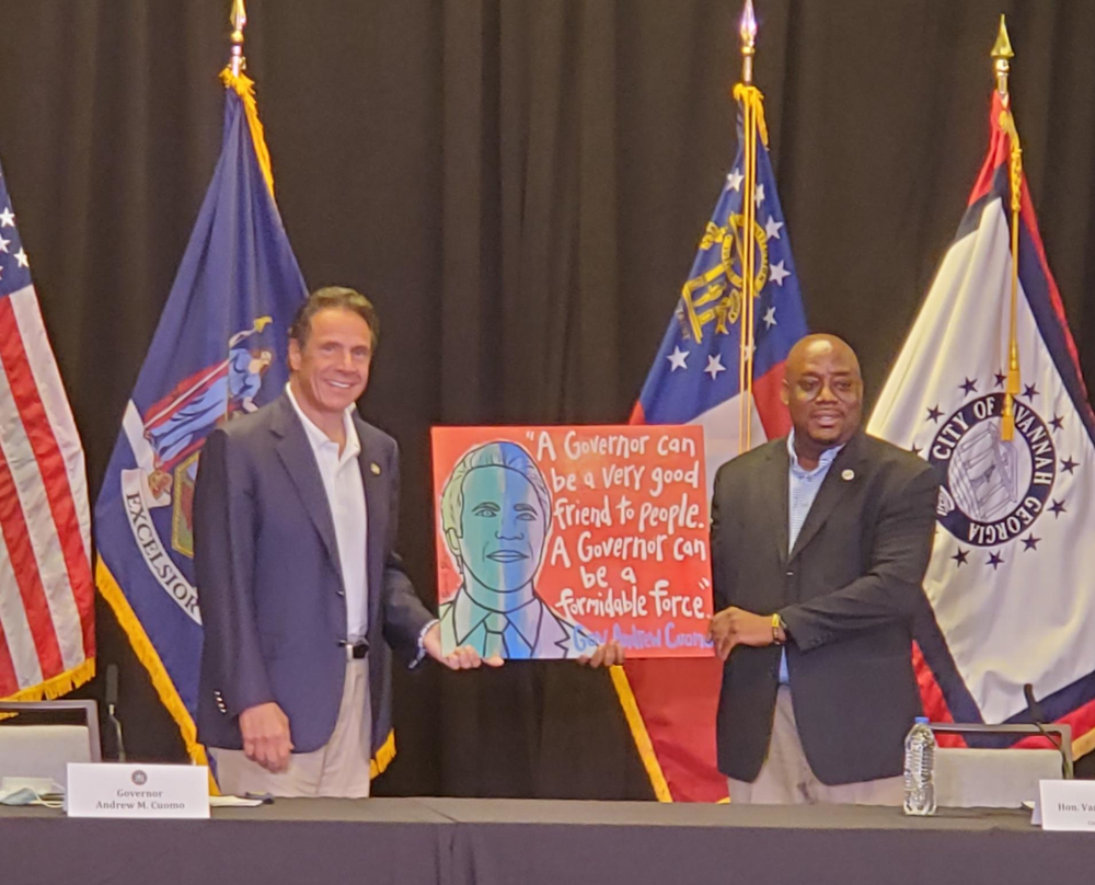 Savannah Mayor Van Johnson presents New York Governor Andrew Cuomo with a painting by local artist Panhandle Slim, featuring Cuomo's picture and a quote.