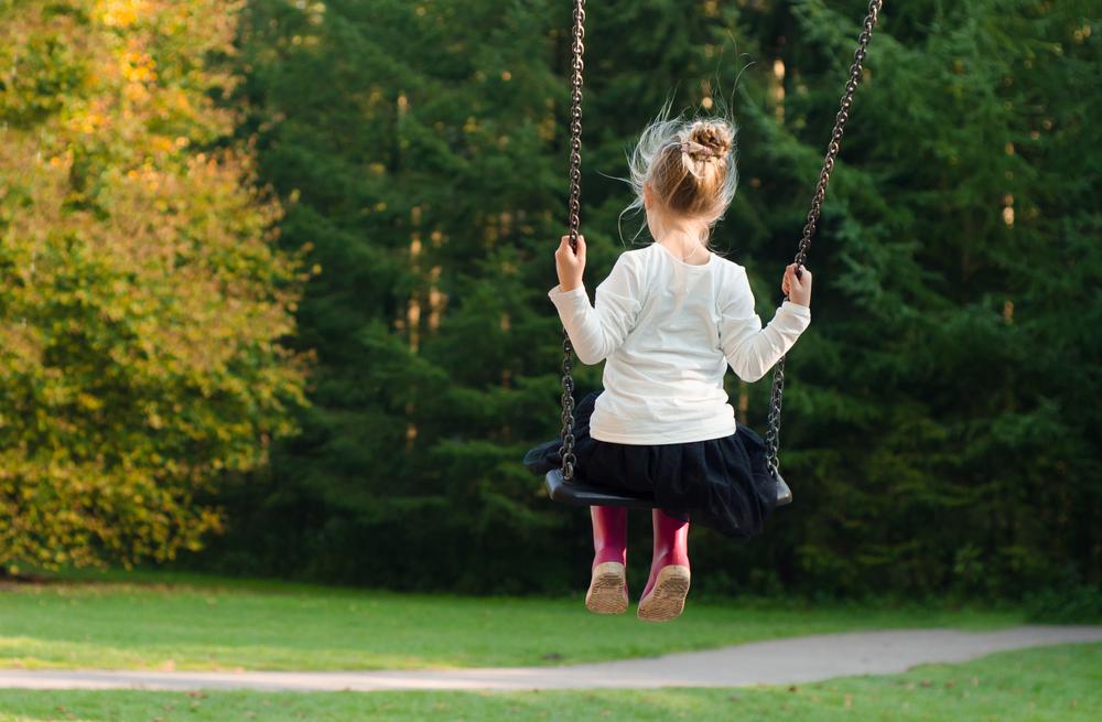 A child wearing pink rain boots uses a swing