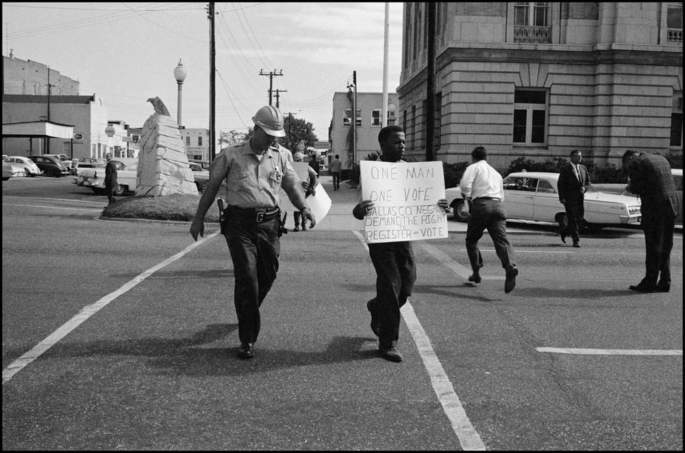 John Lewis holding up a sign that reads "One Man One Vote," advocating for voting rights and voter registration for African Americans.