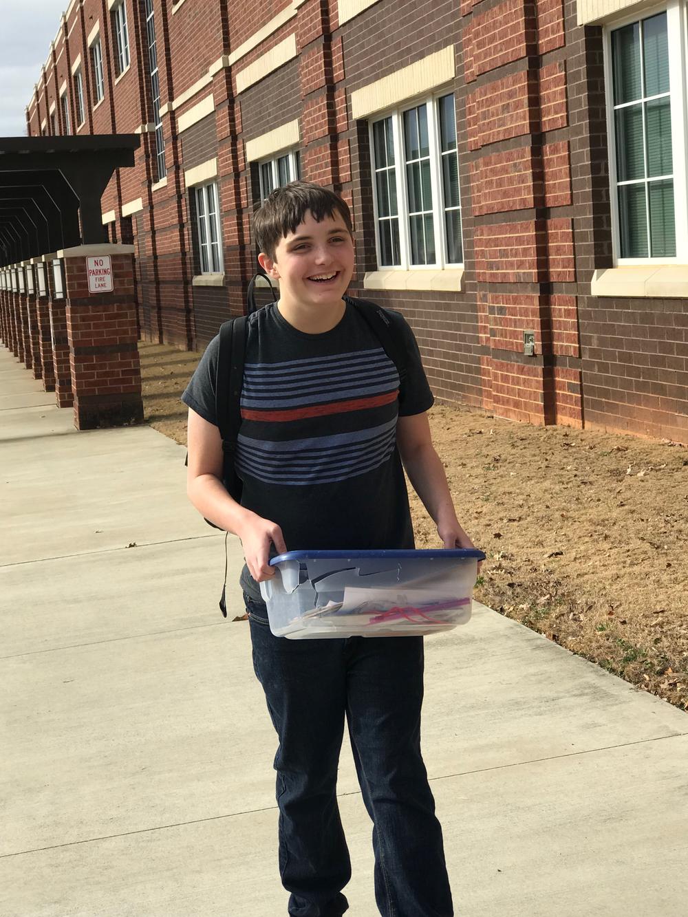 Jack Normanly smiling while holding a clear storage container at his school.