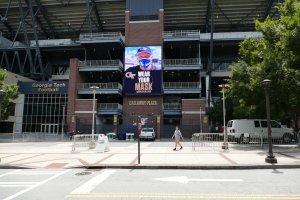 A digital image of Georgia Tech football coach Geoff Collins urges students walking by an entrance to Bobby Dodd Stadium to wear a mask.