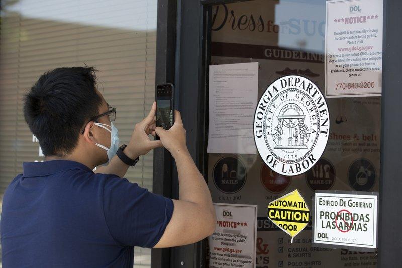 A man uses his phone to copy phone numbers posted on the locked doors of a Georgia Department of Labor office Thursday, May 7, 2020, in Norcross Ga.