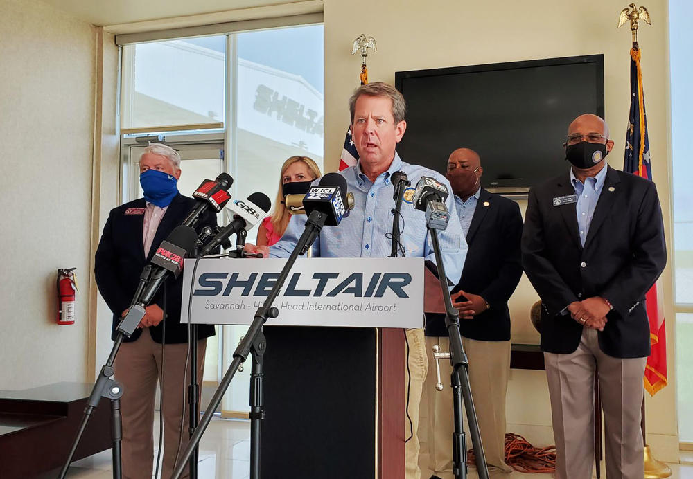 Brian Kemp speaks in Savannah, flanked by local officials.