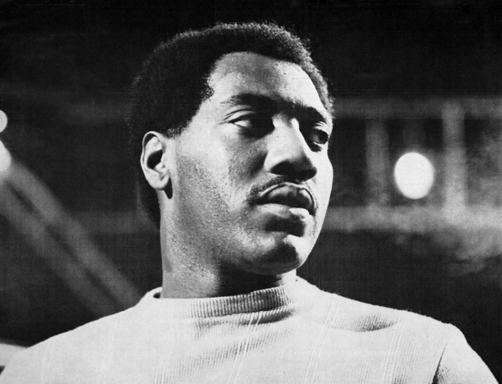 A black and white photo of Otis Redding, looking off-camera to the right, wearing a light sweater.