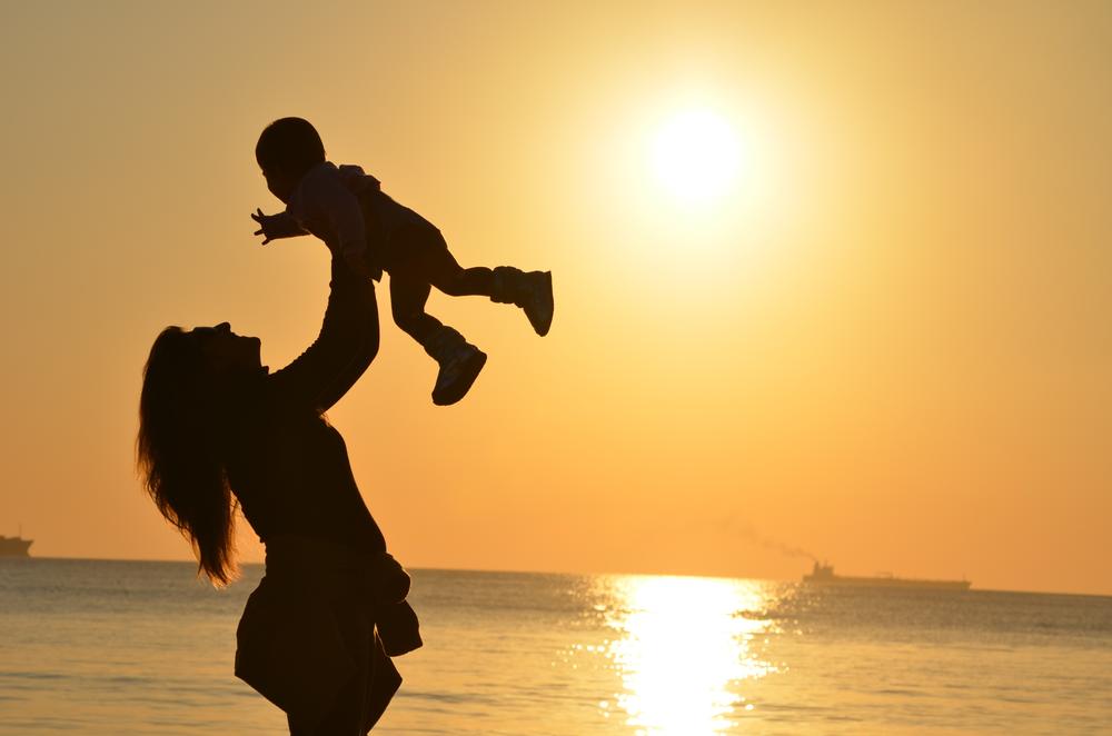 A person holds a toddler up on a beach