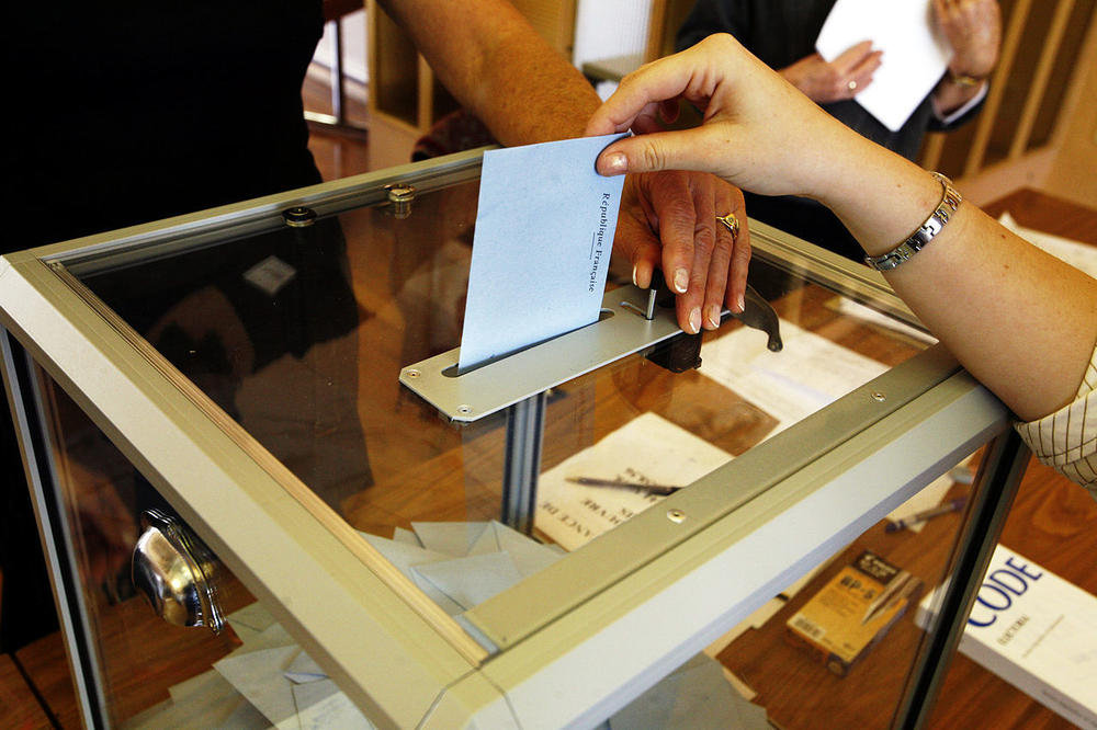 A paper ballot is dropped into a ballot box.