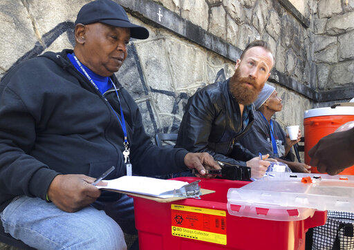 In this photo from March 20, 2019, Harry Ethridge, client services manager at the Atlanta Harm Reduction Coalition, and Jonathan Spuhler, an outreach coordinator for Absolute Care and volunteer at AHRC, set up a needle exchange station for drug users to swap out used syringes for clean syringes on English Avenue in Atlanta.