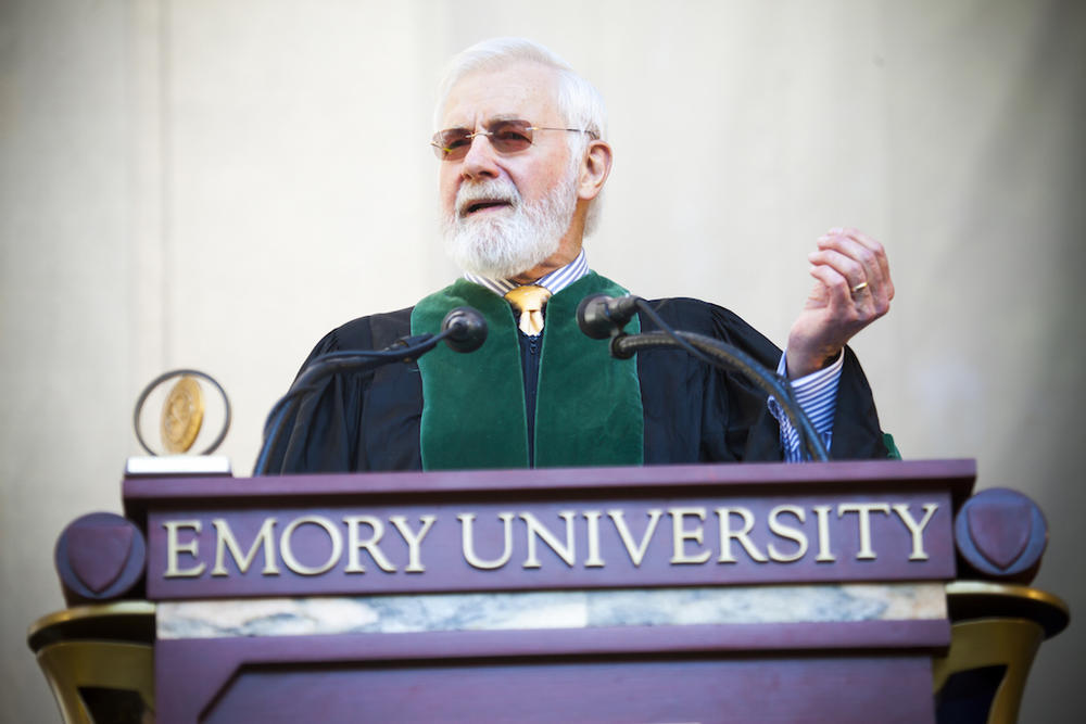 Doctor Bill Foege address a crowd from a fancy pulpit while wearing the collegiate gown.