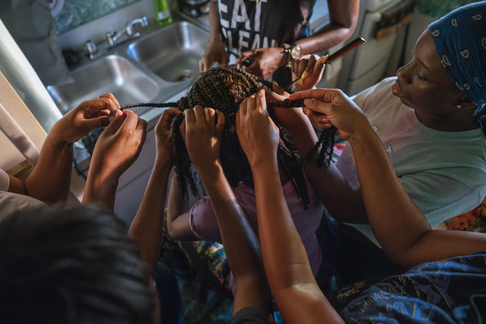 A circle of women collectively braid a young girl's hair.