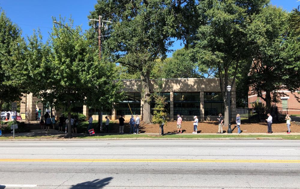 Voters stand in line outside of a library along a road.