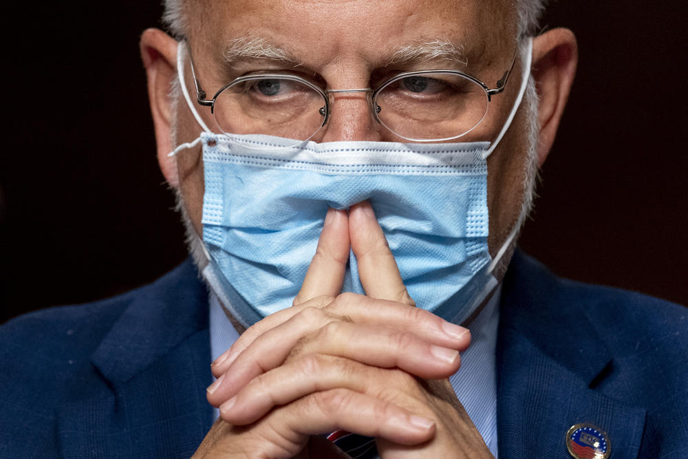 Dr. Robert Redfield wears a mask with his hands in front of his mouth.