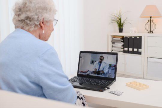 Older woman sitting at computer for telehealth visit.