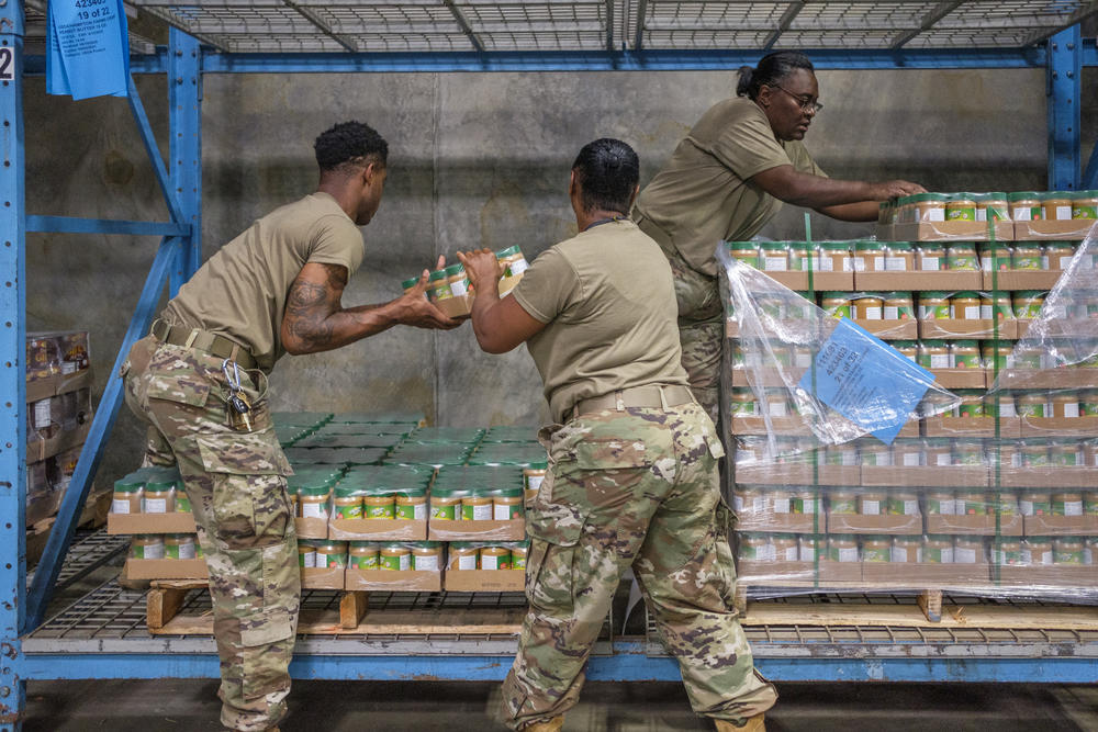 Georgia National Guard members, under the direction of Staff Sergeant Vanessa Williams, right, pull jars of peanut butter for grocery boxes at the Middle Georgia Regional For Bank in Macon. In Georgia, and across the country, Guard members have been taking up the pandemic cause labor slack in food banks. 