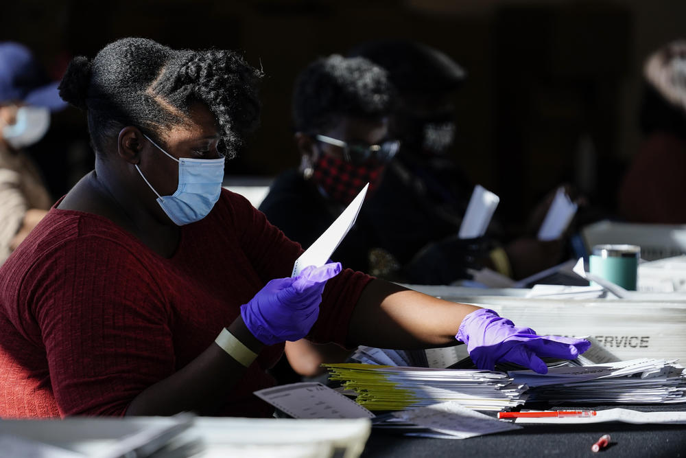 A women counts votes in a starkly lit room.