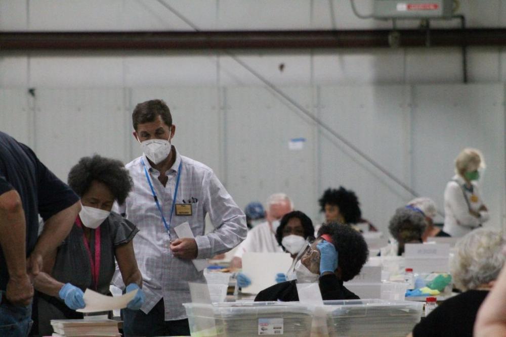 A poll watcher, designated by the yellow badges, interacts with an elections worker.