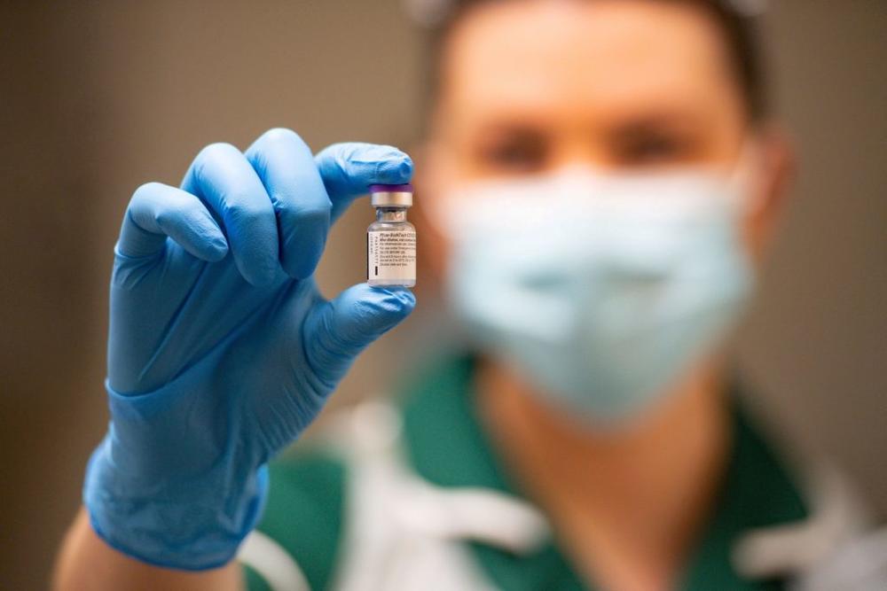 A gloved hand holding a vial of vaccine.