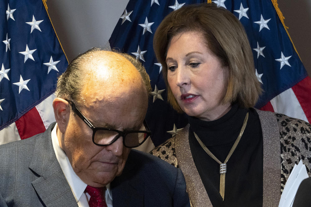 Sydney Powell leans in to whisper to Rudy Guliani.