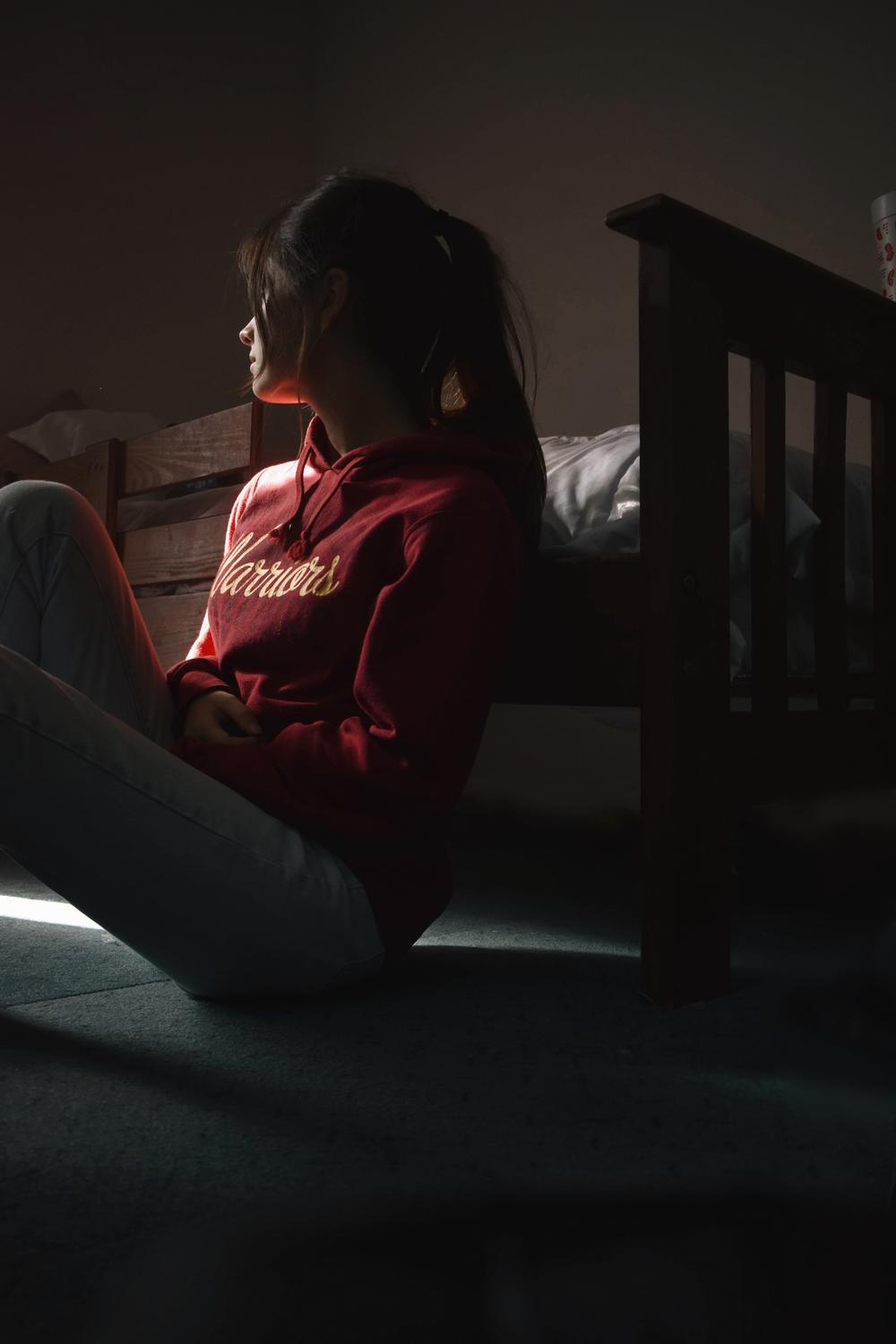 A woman sits on the floor and looks out a window