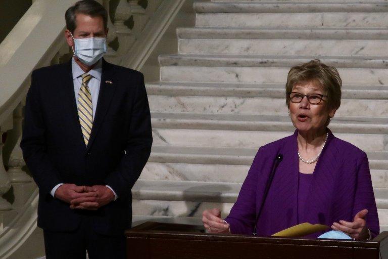 Dr. Kathleen Toomey stands speaking at a press conference on vaccine distribution as Governor Brian Kemp stands behind her.