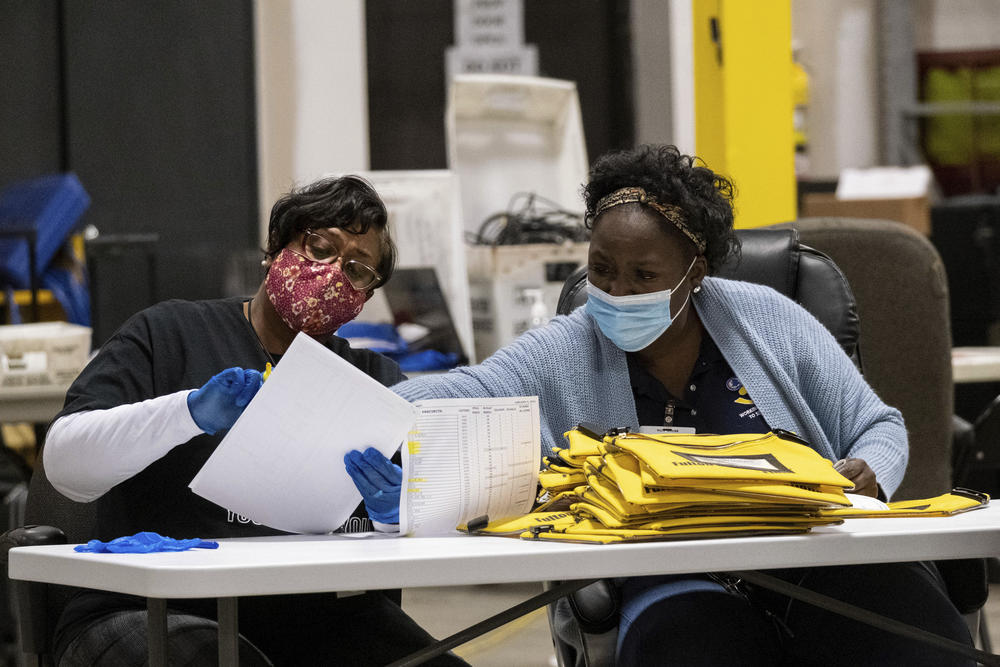 Two women sit at a table looking at a pile of ballots.