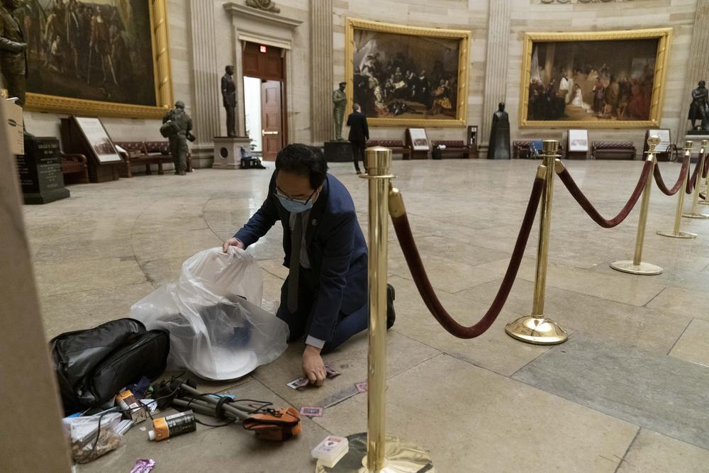 A man in a suit and tie picks up pieces of trash from the floor of the rotunda.