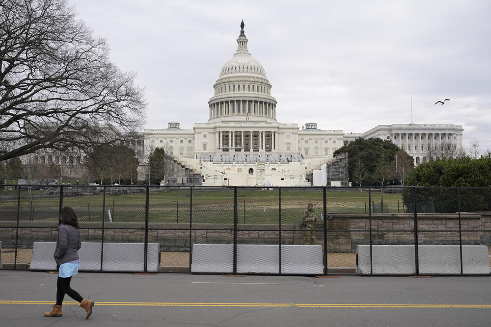 A woman walks past security fencing protecting the West Front of the U.S. Capitol in Washington, Friday, Jan. 8, 2021, as preparations take place for President-elect Joe Biden's inauguration after supporters of President Donald Trump stormed the building.