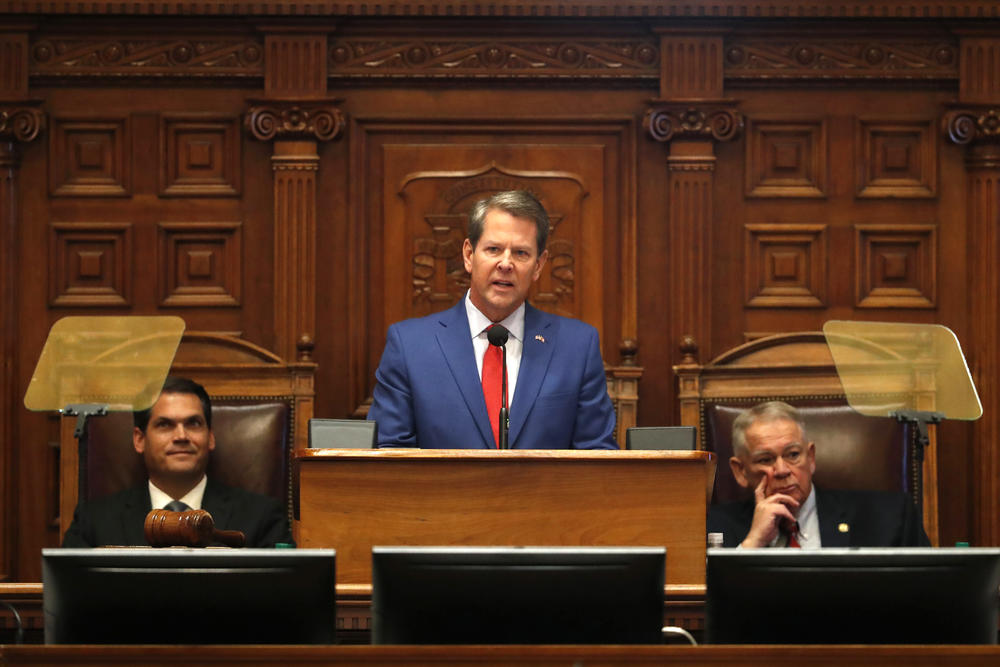 Governor Brian Kemp stands at a lecturn in the General Assembly between David Ralston and Kyle Duncan.