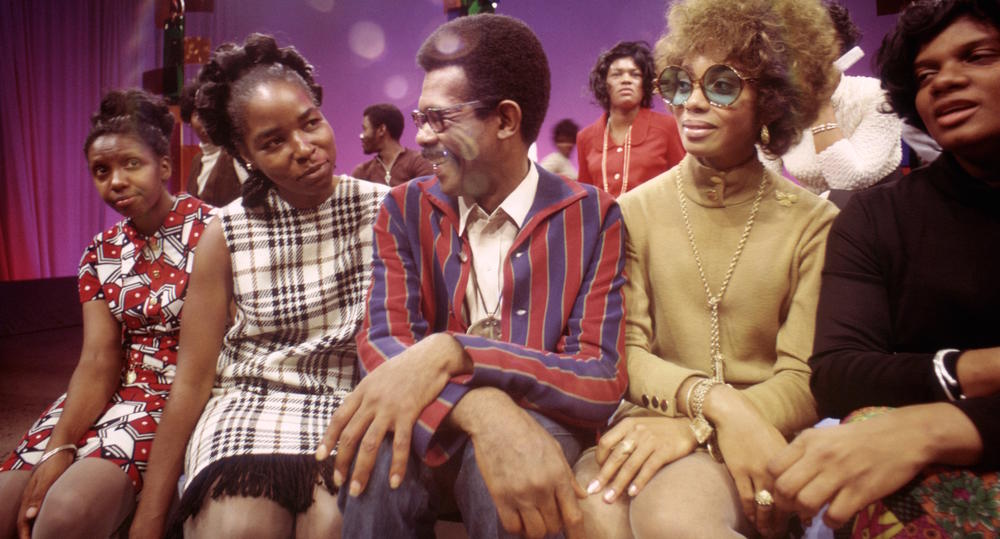A man sits between 4 women on a soundstage.