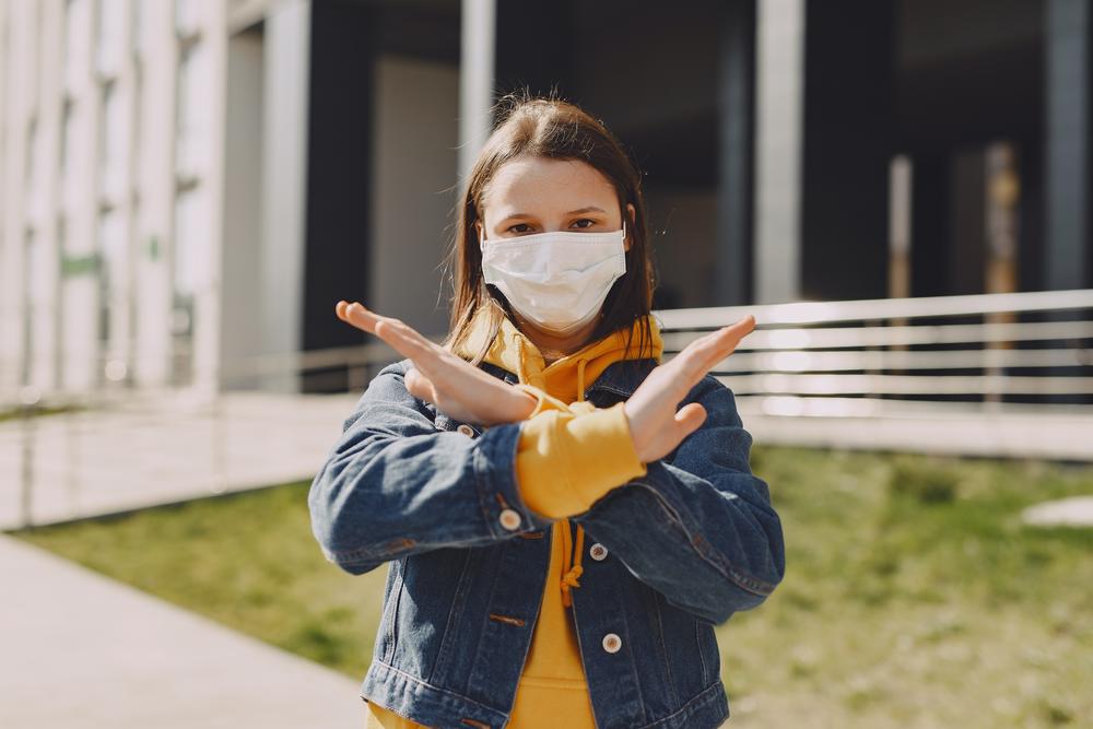 A girl in a face mask shows the sign for stop.