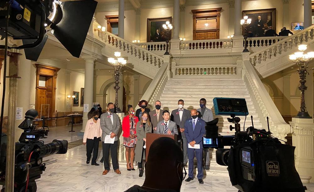 A group of lawmakers stand in the General Assembly addressing press during a news conference.