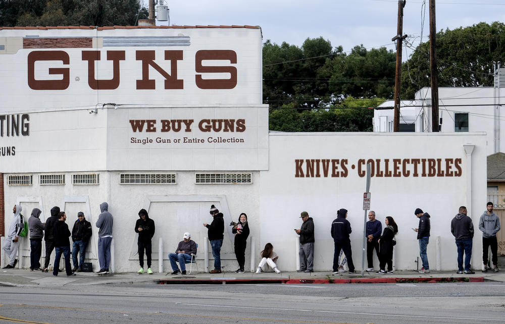 Folks stand in a line outside of a store selling guns.