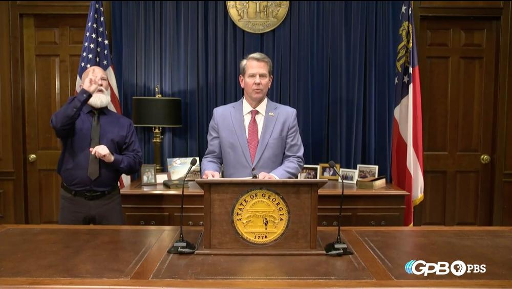 Governor Brian Kemp stands in the general assembly speaking to a camera.