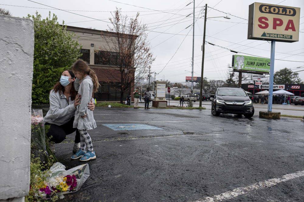 A mother and daughter stand by a memorial outside of the Gold Spa.