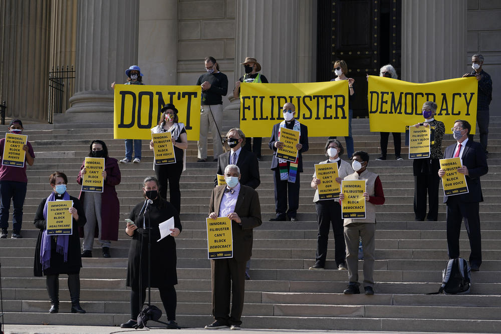 Protestors stand with signs.