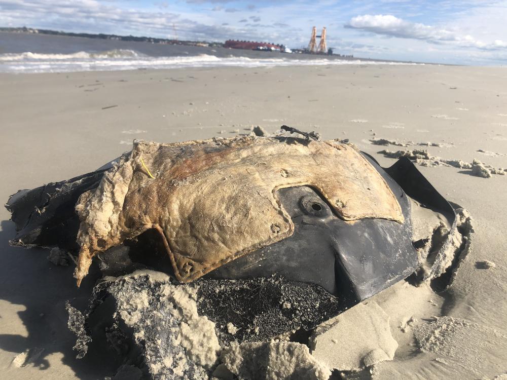 a car fuel tank washed up on a beach, the Golden Ray wreck in the background