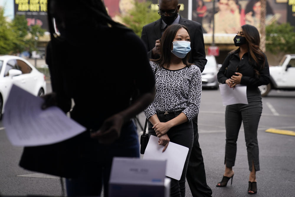 People wait in line, resumes in hand, while waiting to apply for jobs during an outdoor hiring event.