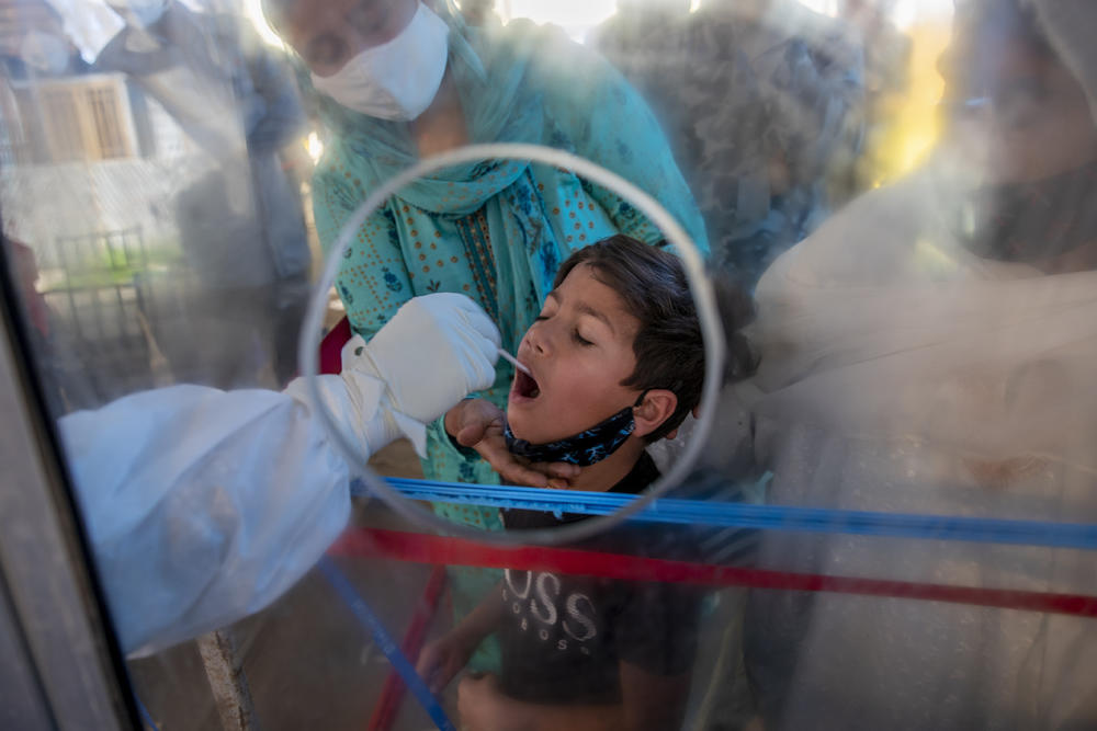 A boy in India is tested for COVID-19 through a plastic screen.