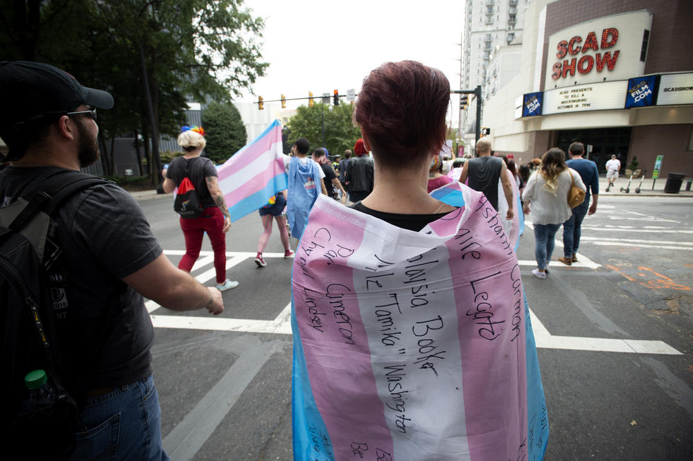 A supporter for the transgender and non-binary community, wearing a transgender flag with handwritten names of black trans women who the person said were killed in 2019, strolls through the city's Midtown district during Gay Pride Festival's Transgender Rights March in Atlanta on Saturday, Oct. 12, 2019.