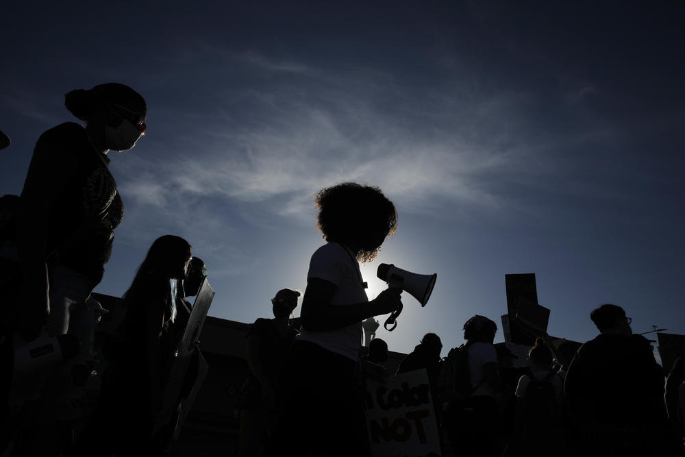 A group of protestors stand silhouetted by the sun.