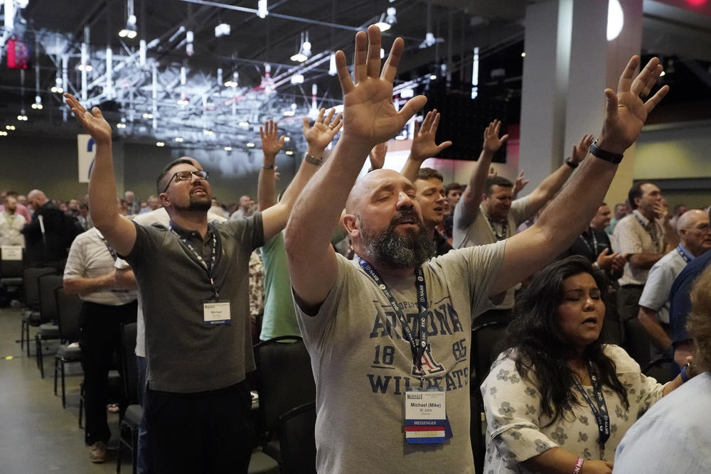 A crowd of worshippers stand with their arms raised at the Southern Baptist Convention.