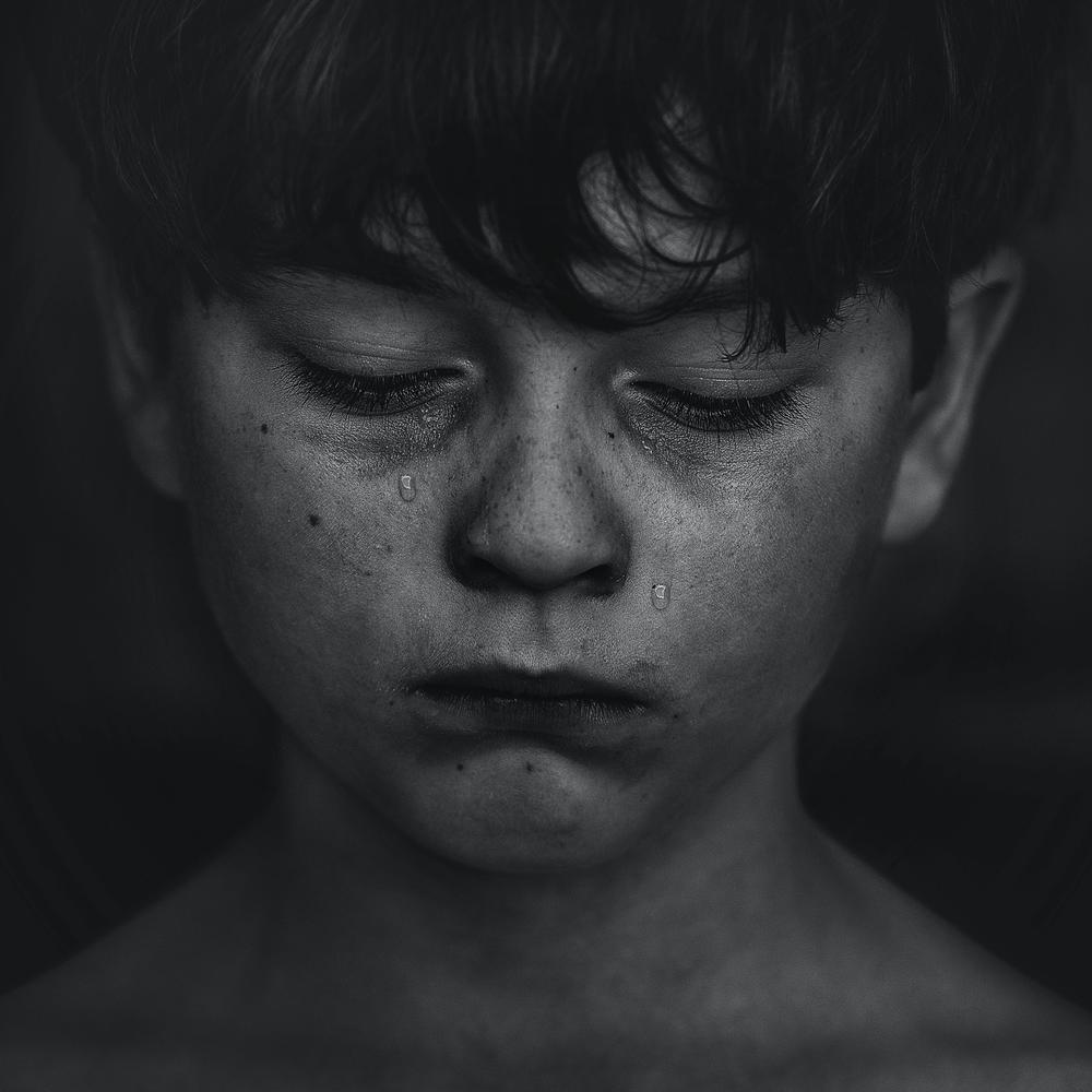 A boy with tears on his face looking down