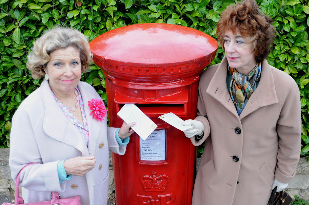 Two women standing next to a mailbox.