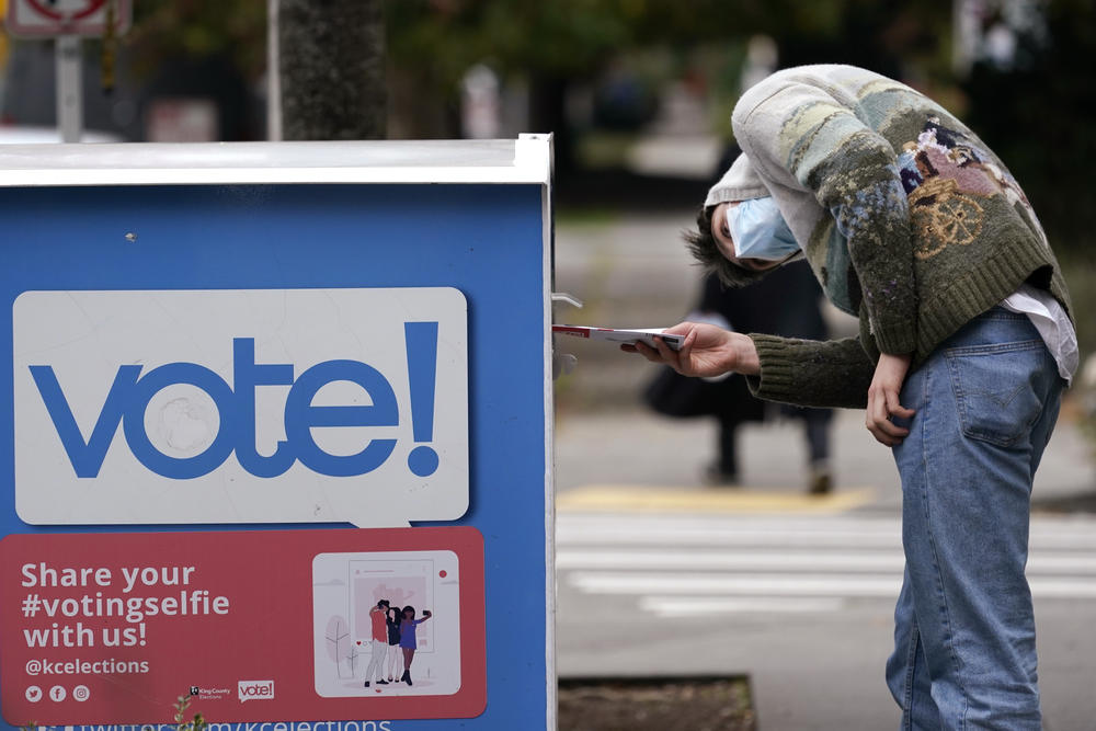 In this Oct. 28, 2020, file photo, a voter turns sideways as he eyes the opening of a ballot drop box before placing his ballot inside it in Seattle. 