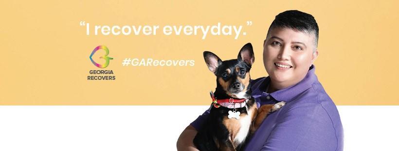 Recovery billboard says "I recover everyday" with a person in a purple shirt holding a dog.