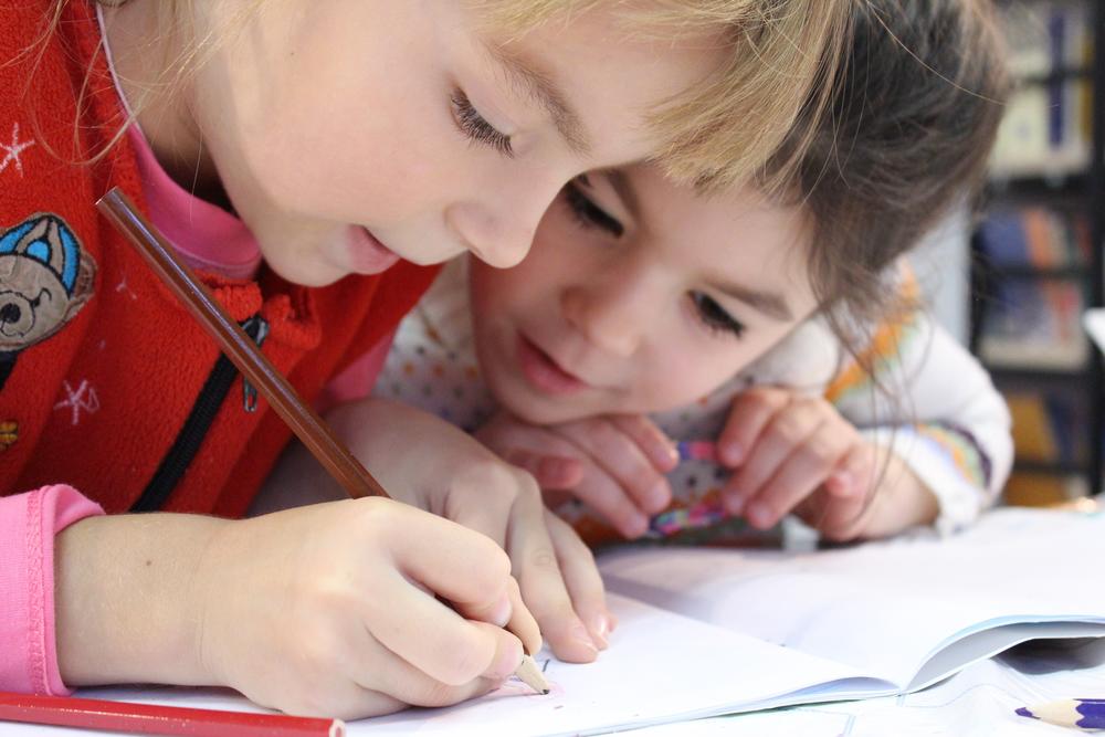 Preschool girls at a desk, looking at a notebook