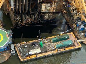 An oil recovery team uses a floating vacuum attachment connected to green containers to pump out oil that discharged from Section Six during lifting operations on Wednesday. 
