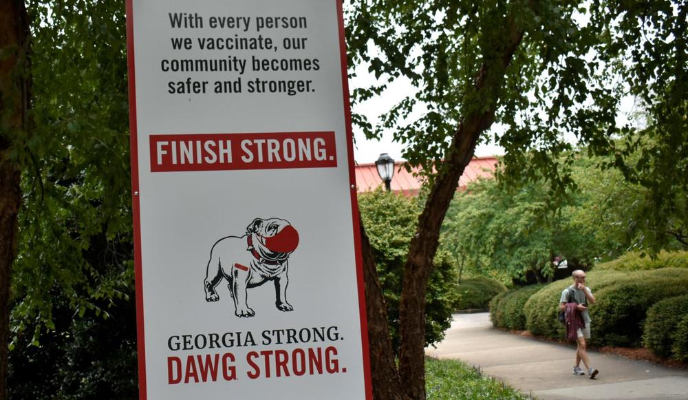 A sign at the University of Georgia encourages students to vaccinate and mask up. Some professors want face coverings to be required.