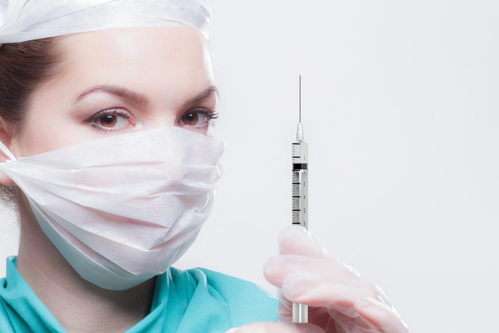 woman healthcare professional in mask holds a vaccine syringe