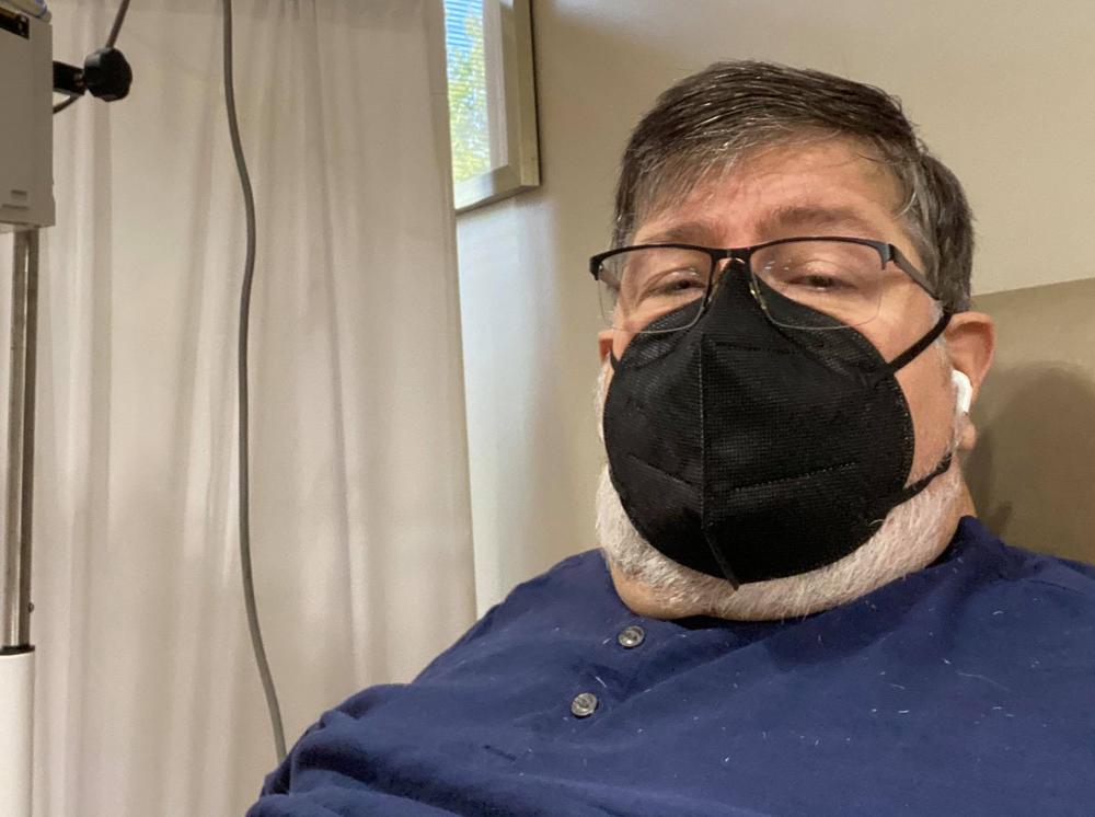 Dennis Loubiere in a black face mask while receiving an infusion of monoclonal antibodies