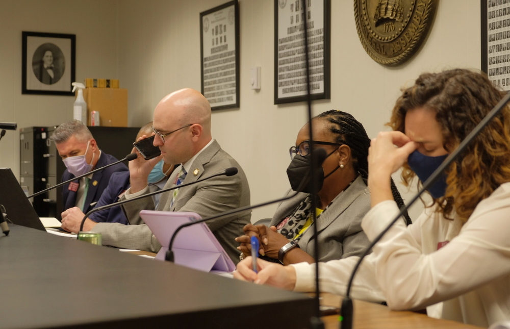 Georgia House Member Josh McLaurin (D-Sandy Springs) holds his phone to a microphone so other members of a committee on conditions in Georgia prisons can hear anonymous testimony from a guard at Lee Arrendale State Prison.